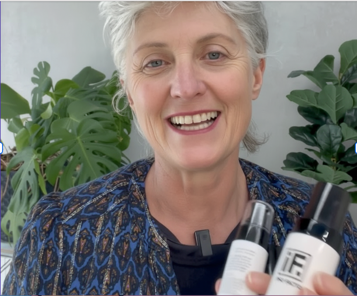 Smiling woman holding two small batch skincare bottles in front of indoor plants