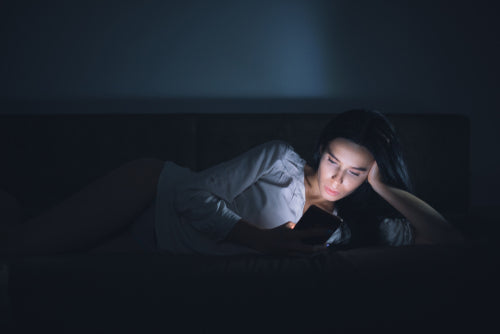 Woman lying on a couch in dim light, looking at her phone, relaxed evening skincare routine