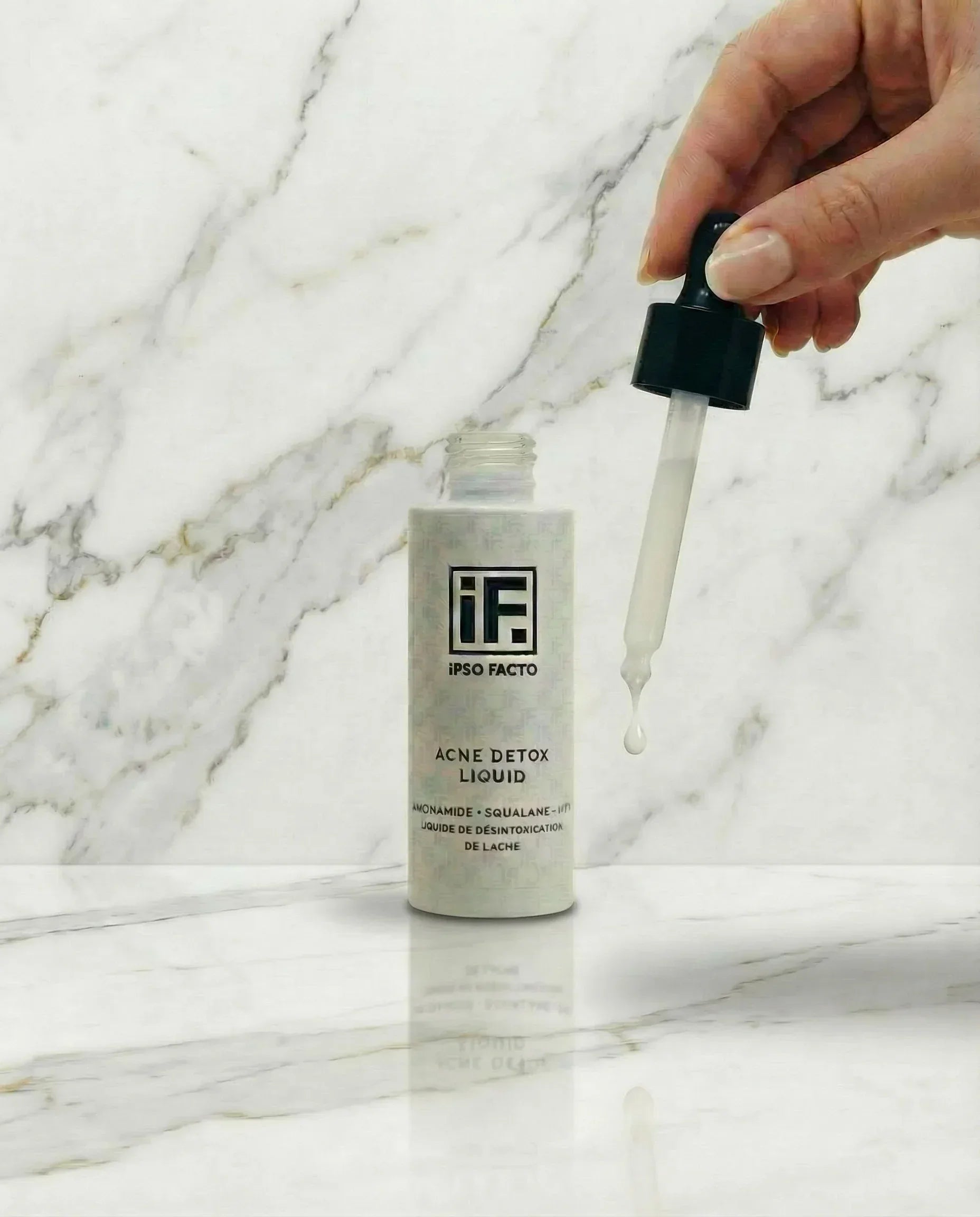 Hand holding dropper above Acne Detox Liquid skincare serum bottle on marble surface