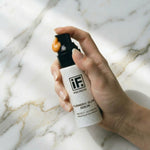 Hand holding IF Turmeric Glow Serum bottle with golden serum on pump, white marble background
