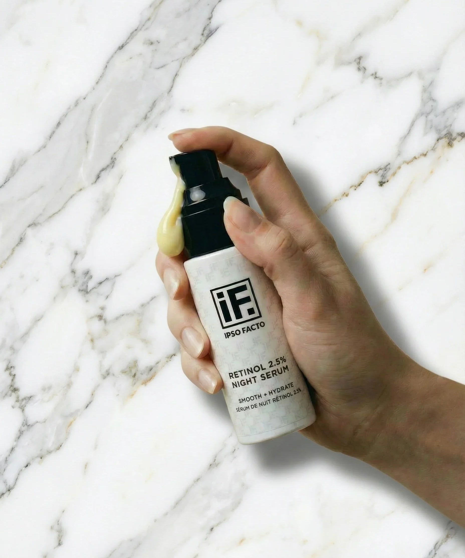 Hand holding retinol 2.5% night serum bottle on white marble background