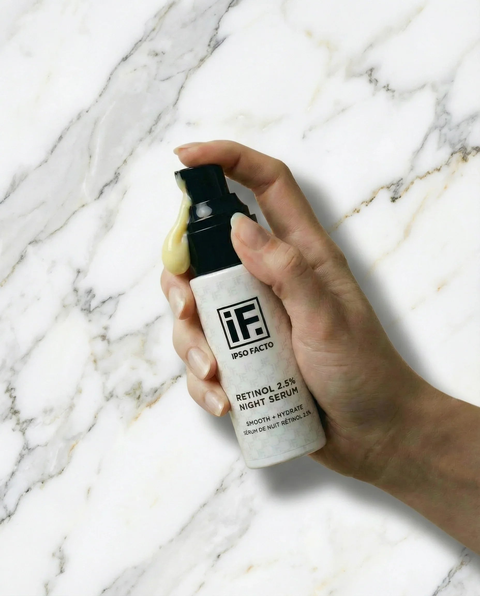 Hand holding retinol 2.5% night serum bottle on white marble background